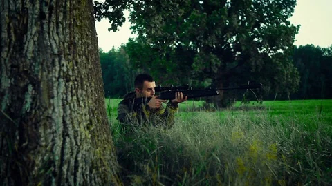 Hunter sitting under a tree and aim at prey Stock Footage 94305297