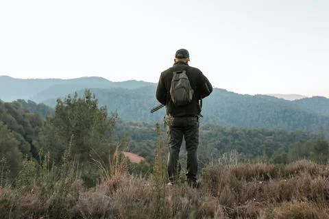 Hunter standing on top of mountain range looking downhill Stock Photos