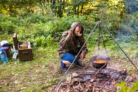 Hunter tasting stew cooked on bonfire in forest Stock Photos