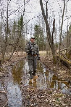 A hunter wades through a puddle on a forest road Stock Photos