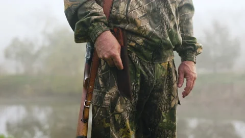 A hunter with a weapon slowly gets out of his knife near a misty lake Video stock 196620603