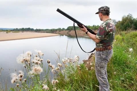 A hunter with a weapon stands on the river side Stock Photos