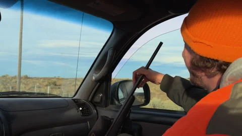 Hunter wearing an orange jacket sitting as a passenger during Mule Deer hunting Stock Footage 304597020
