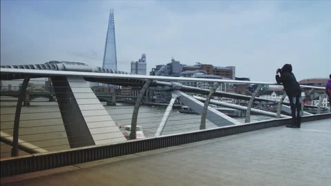 Hurrying passersby walk on the Millennium Bridge, an elegant steel walkway. Stock Footage 296072093