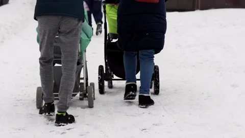 A husband and wife and a stroller with a child walk along a snowy sidewalk in Stock Footage 293684053