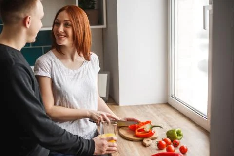 The husband is standing in the kitchen next to his wife when she is cooking.  Stock Photos