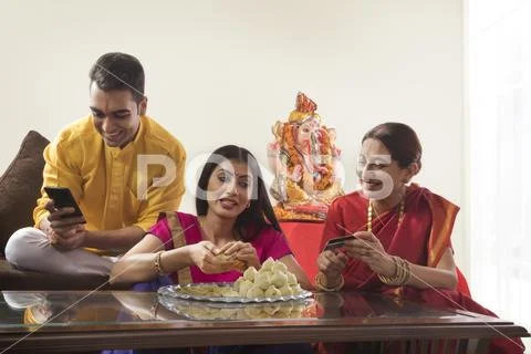 Husband wife sitting together while wife makes modaks and mother in law holds a Stock Photos
