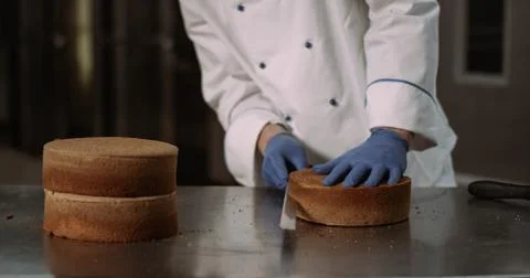 A husky good looking baker guy with proper chefs attire cuts the cake in half Stock Photos
