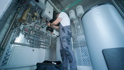 HVAC Technician Adjusting Heat Pump and Boiler System in Modern Mechanical Room Stock Footage 340112473