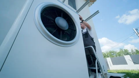 HVAC technician on a ladder installing a large outdoor heat pump unit Stock Footage 340112738