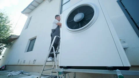 HVAC technician on a ladder installing a large outdoor heat pump unit Stock Footage 340112882