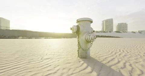Hydrant standing alone in sandy area during golden hour near buildings Ilustración de archivo