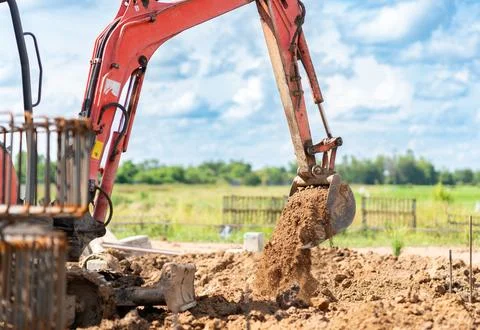 Hydraulic arm of a mini digger scooping and moving brown dirt for ground le.. 스톡 사진