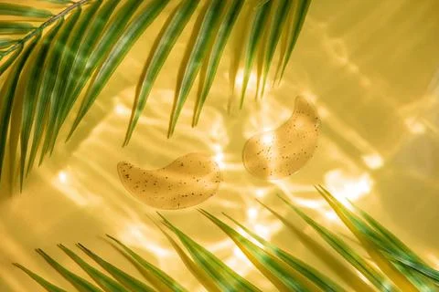 Hydro gel eye patch on yellow background with palm leaves and water highlight Stock Photos