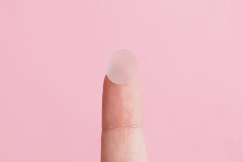 Hydrocolloid acne patch on fingertip over pink background Stock Photos