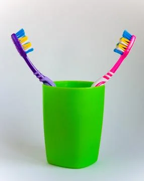 Hygiene. Two multi-colored toothbrushes stand in a green glass. Stock Photos