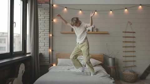 Hyperactive child boy jumps on bed imagining like fly in air, have fun alone Stock Footage 267225694