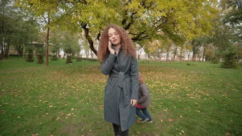 Hyperactive child running around young mother, talking on phone, wants attention Stock Footage 144318096