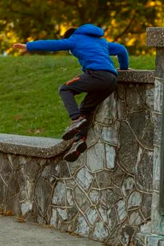 A hyperactive kid is jumping off a high wall as he is running away. Stock-Fotos