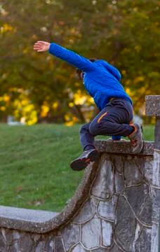 A hyperactive kid is jumping off a high wall as he is running away. Stock Photos