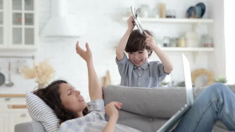 Hyperactive son disturb tired mom lying on sofa in living room with laptop work Stock Footage 156821358