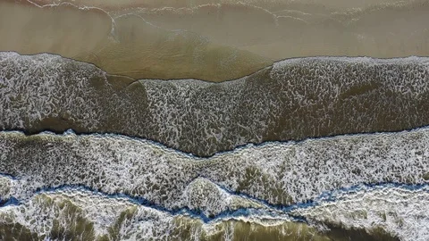 Hypnotic drone footage of waves rolling over flat sandy beach Stock Footage 114199429