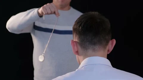 The hypnotist introduces the patient into a state of hypnosis with a pendulum 動画素材 168572353