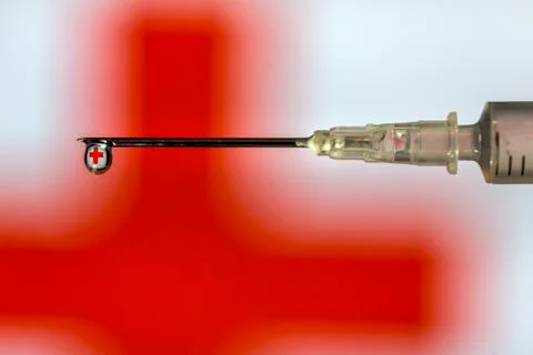 Hypodermic needle dripping fluid with red cross reflected over a red and whit Stock Photos