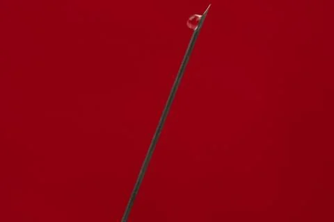 Hypodermic needle of a syringe with a drop, closeup isolated on red backgroun Stock Photos