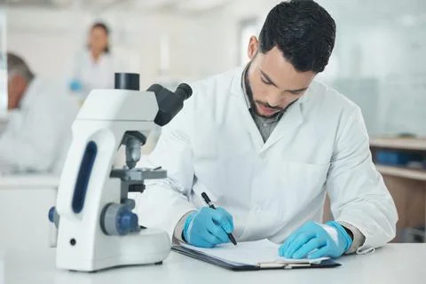 I better record that. a young scientist writing notes while using a microscope Foto stock