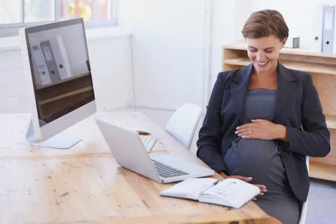 I cannot wait to meet you. A pregnant businesswoman smiling affectionately at Foto stock