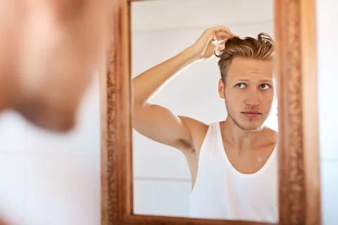I could do with a makeover. a young man looking at his hair in the mirror at Stock Photos