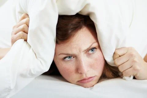 I dont wanna get up. A grumpy looking woman lying in bed with a pillow over her Stock Photos