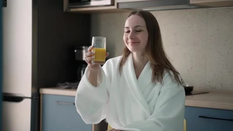 I enjoy a well-balanced breakfast. A smiling woman in a bathrobe drinks orange Stock Footage 252660080