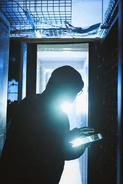 I work best in the dark. a hacker using a digital tablet in a server room. Stock Photos