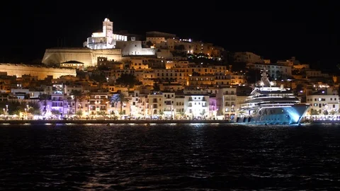Ibiza old town at night ablaze with colour across dark water Stock Footage