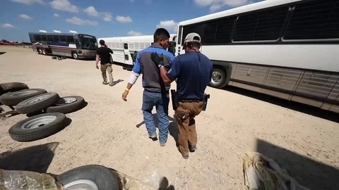 ICE agent escorts suspect illegal migrant worker towards waiting coach Stock Footage 94324338