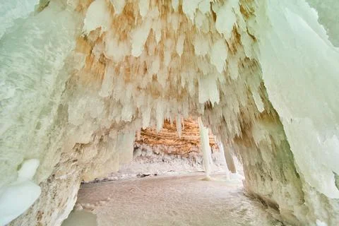 Ice cavern covered in small icicles and frozen lake on the ground Stock Photos