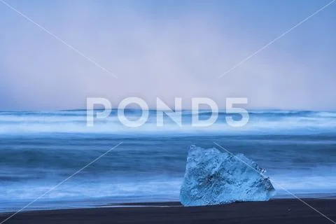 Ice chunk on the shore of the ocean with waves crashing against the shoreline Stock Photos