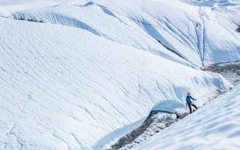 Ice climber abseiling down steep ice slope so his friends can climb up from b Stock Photos