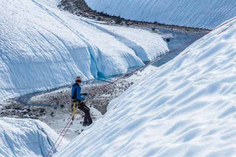 Ice climber rappelling down a slope into rocky canyon on the Matanuska Glacie Stock Photos