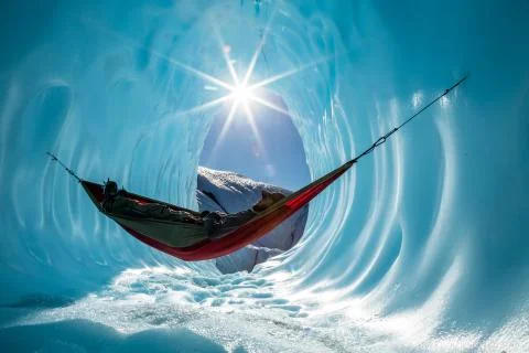 Ice climber rests in hammock inside ice cave in the Alaskan wilderness Stock Photos