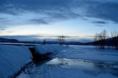 Ice covered river stream and snowy field in winter blue hour Stock Photos