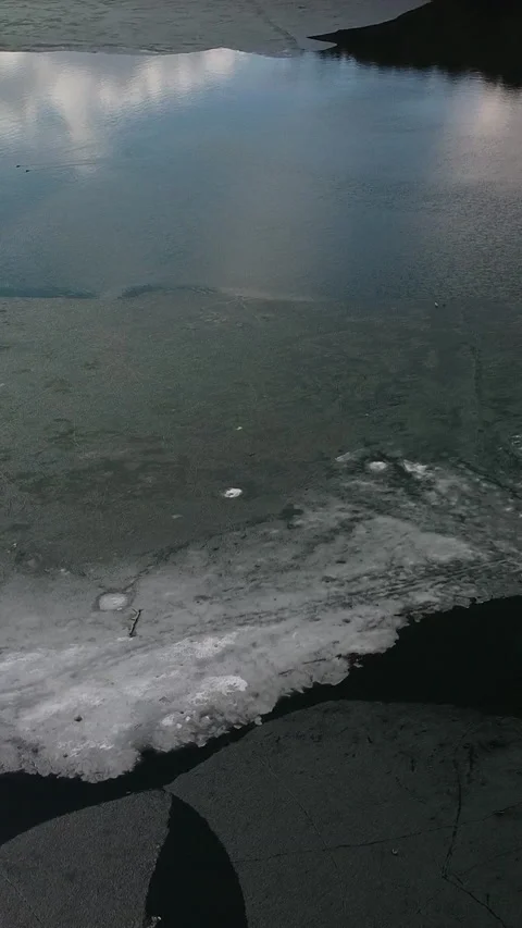 Ice cracks drift across dark water's surface Video stock 347499392