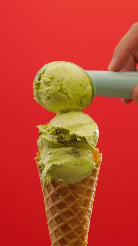 Ice cream scooping. Scoop green ice cream on a vibrant red background. Vertical Stock Footage 311546230