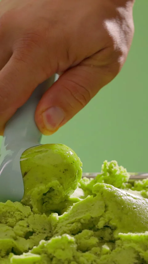 Ice cream scooping. Scoop green ice cream on green background. Summer refreshing Stock Footage 314136489
