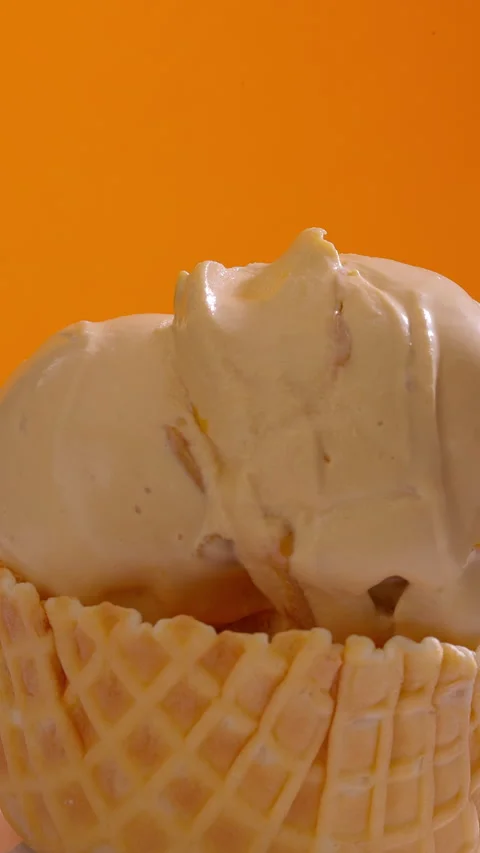 Ice cream scoops stacked into waffle cone on orange background. Vertical close Stock Footage 313164629