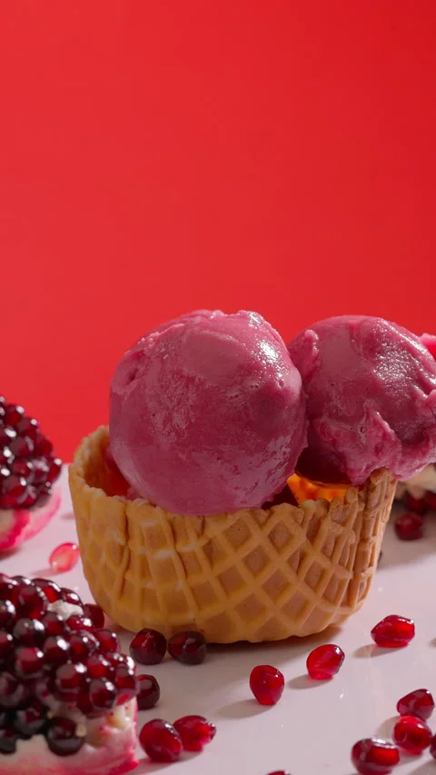 Ice cream scoops stacked into waffle cone surrounded by pomegranate seeds Stock Footage 314133016