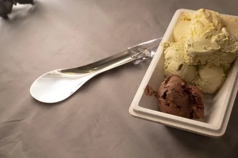 Ice cream served on a table with a plastic container and metal spoon, top-down. Stock Photos