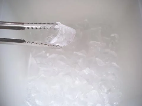 An Ice Cube being held by Silver Tongs above an Icebox Stock Photos